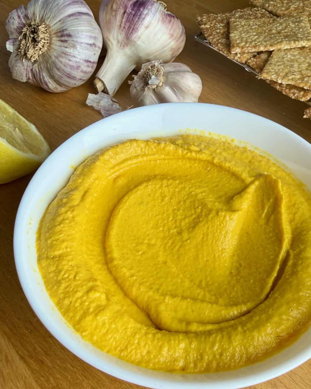 Creamy roasted carrot dip with tahini and garlic on a wooden surface.