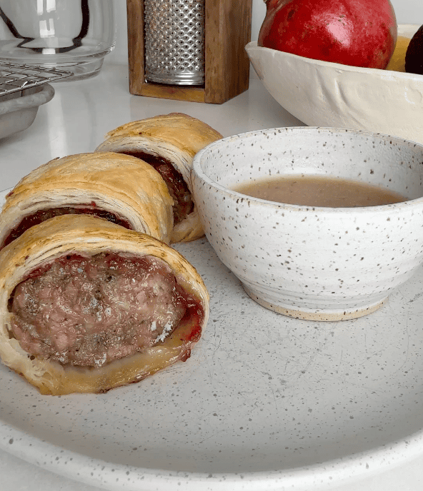 A few sausage rolls on a plate with a side of gravy for dipping.