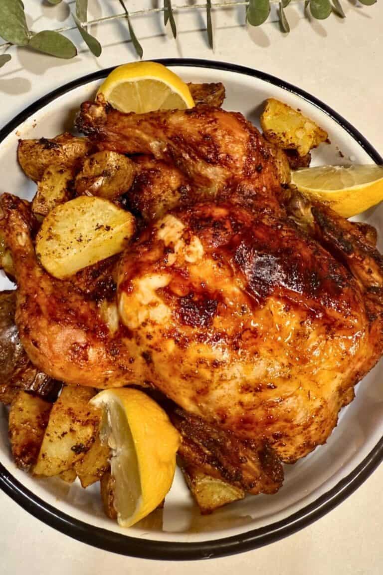 Air fryer whole chicken with potatoes and lemons on a white serving dish.