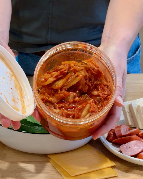 A woman holds a large container of kimchi.