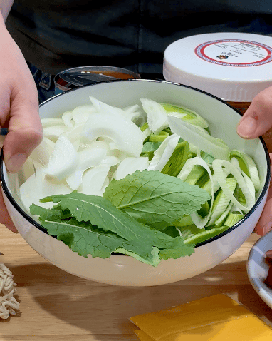Fresh vegetables for Budae Jjigae recipe, including onions and leafy greens.