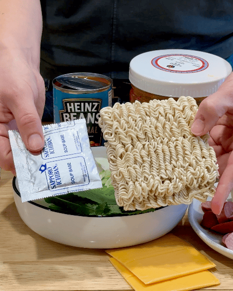A woman holds a packet of ramen and seasoning.