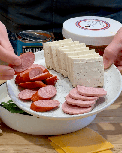 A woman holds a plate of tofu, sausage, and spam.