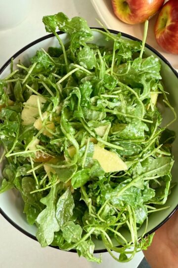 A woman holding a serving bowl with the finished arugula salad.