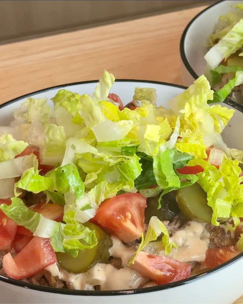 Adding lettuce to the cheeseburger bowl.