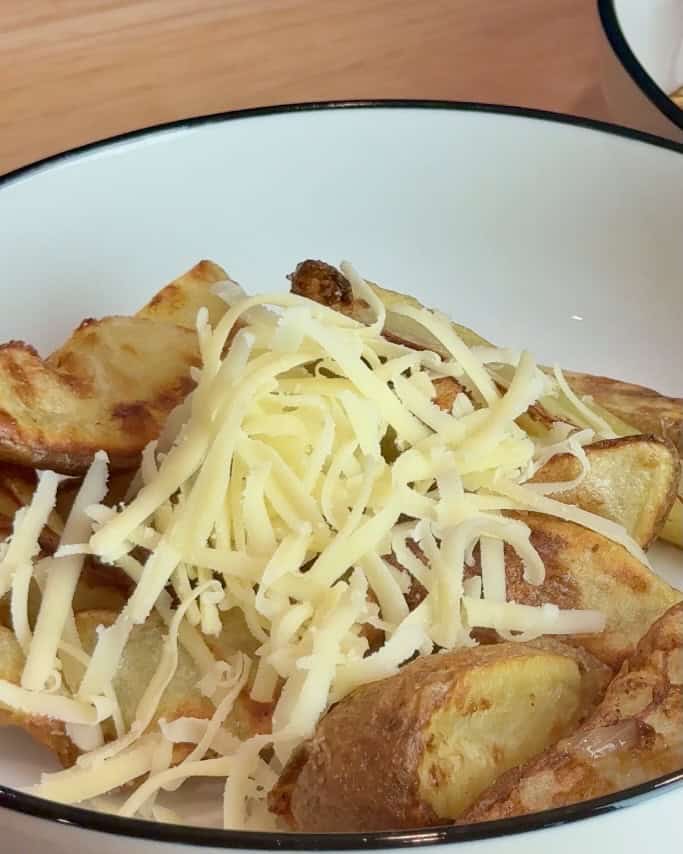Layering grated cheese over the wedge fries.