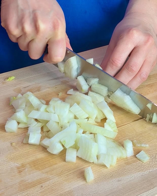 A woman chops onions on a wooden cutting board.
