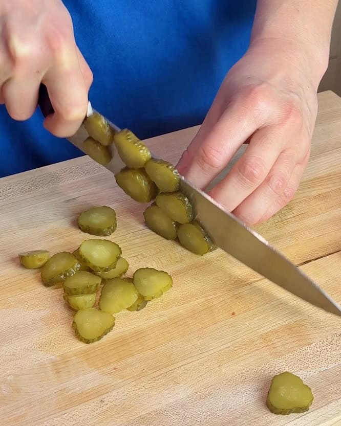 A woman slices dill pickles on a wooden cutting board.