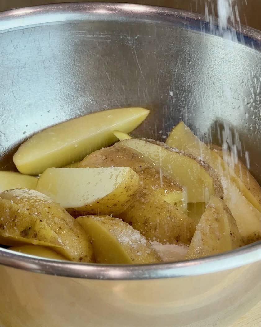 Sprinkling salt over potato wedges and tossing in a bowl.