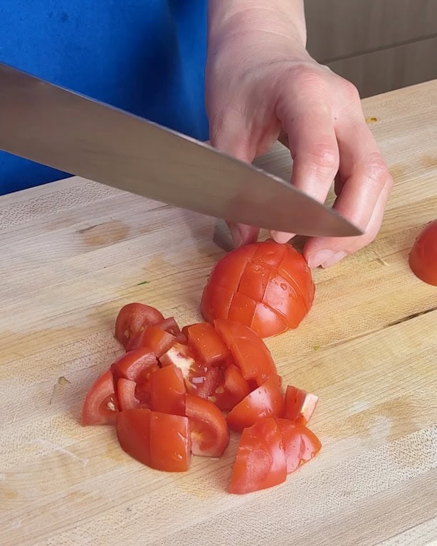A woman chops tomatoes on a wooden cutting board.