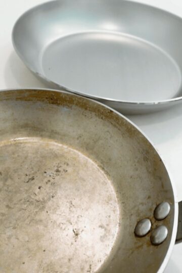 A seasoned carbon steel pan next to a brand new carbon steel pan.