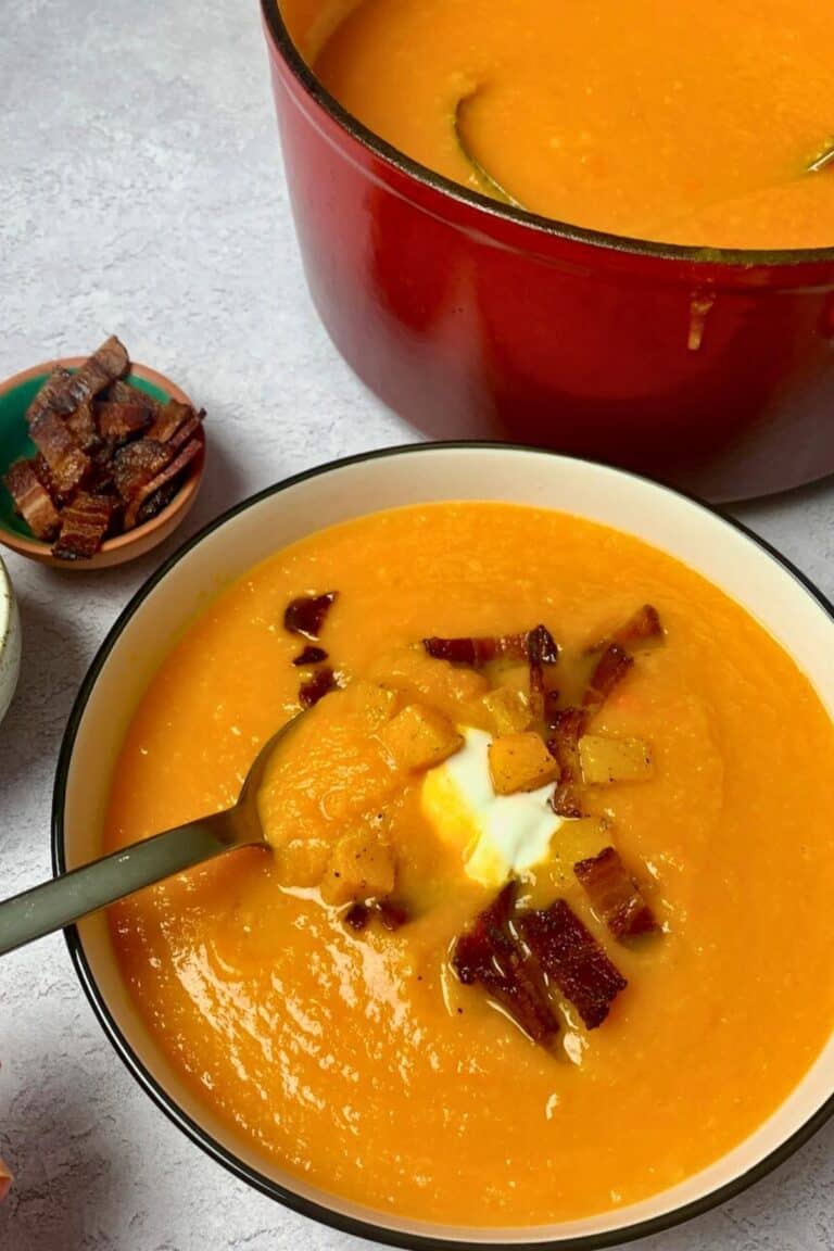 A spoonful of finished carrot butternut squash soup, garnished with sour cream, bacon, and cubed roasted squash.