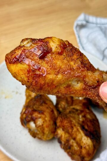A woman holding an air fryer chicken drumstick over a plate.