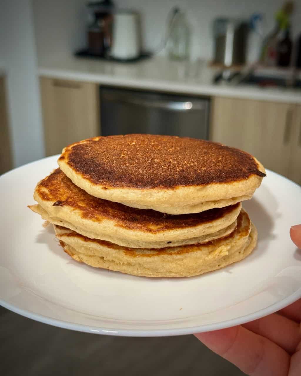 A woman holds a white plate with a stack of cottage cheese pancakes made with oat flour.