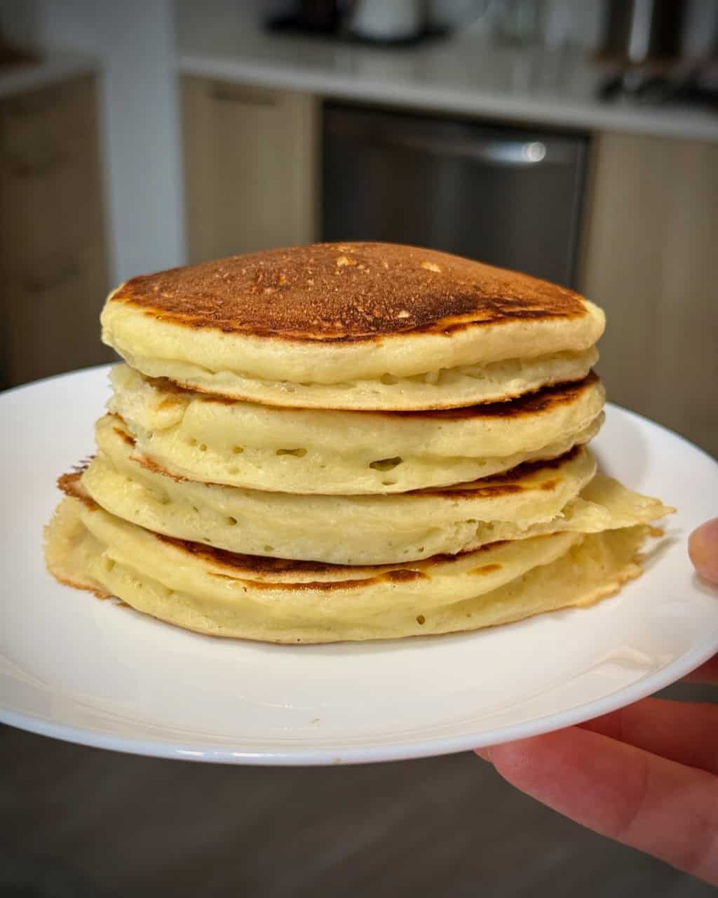 A woman holds a white plate with a stack of cottage cheese pancakes.