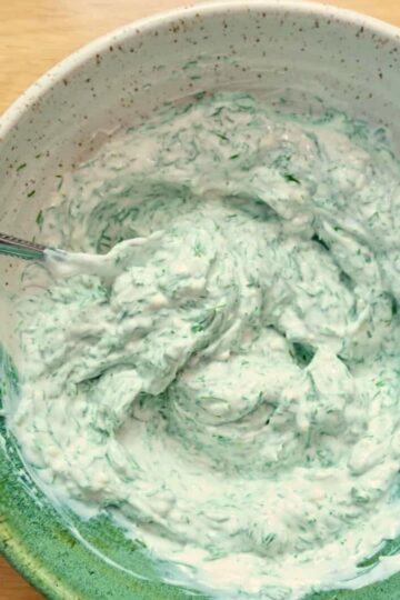 A bowl of creamy yogurt dill sauce with a spoon.