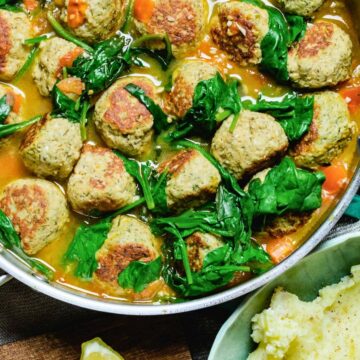 a pan of turkey meatballs in broth with wilted spinach.