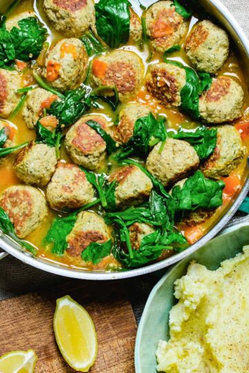 a pan of turkey meatballs in broth with wilted spinach.