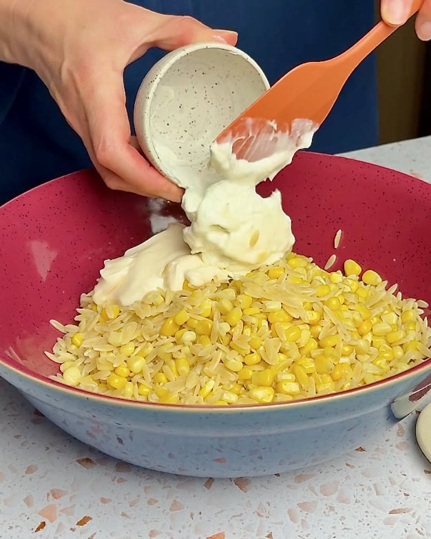 Adding creamy mayonnaise to the corn and pasta.