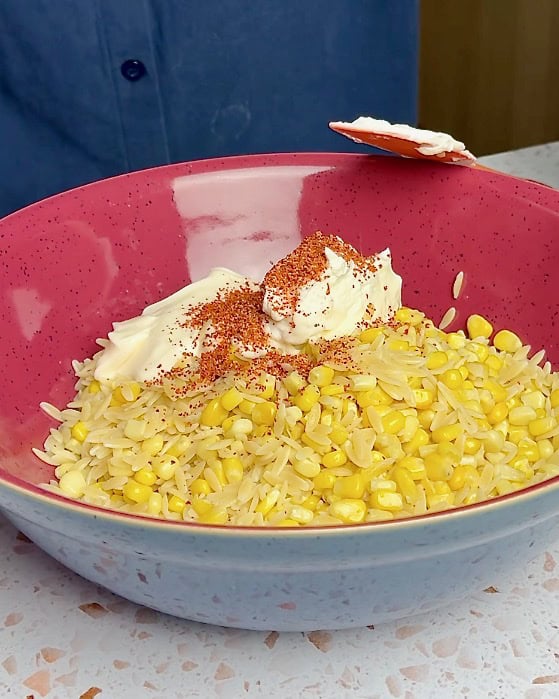 Adding the dressing ingredients to the corn and pasta.