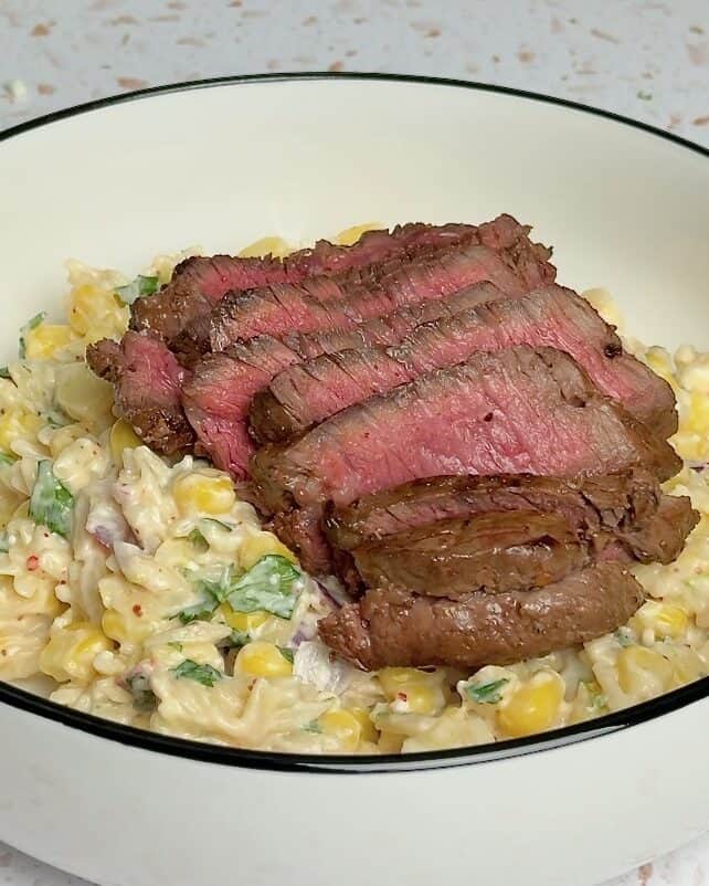 Elote pasta salad in a white bowl, topped with seared steak.