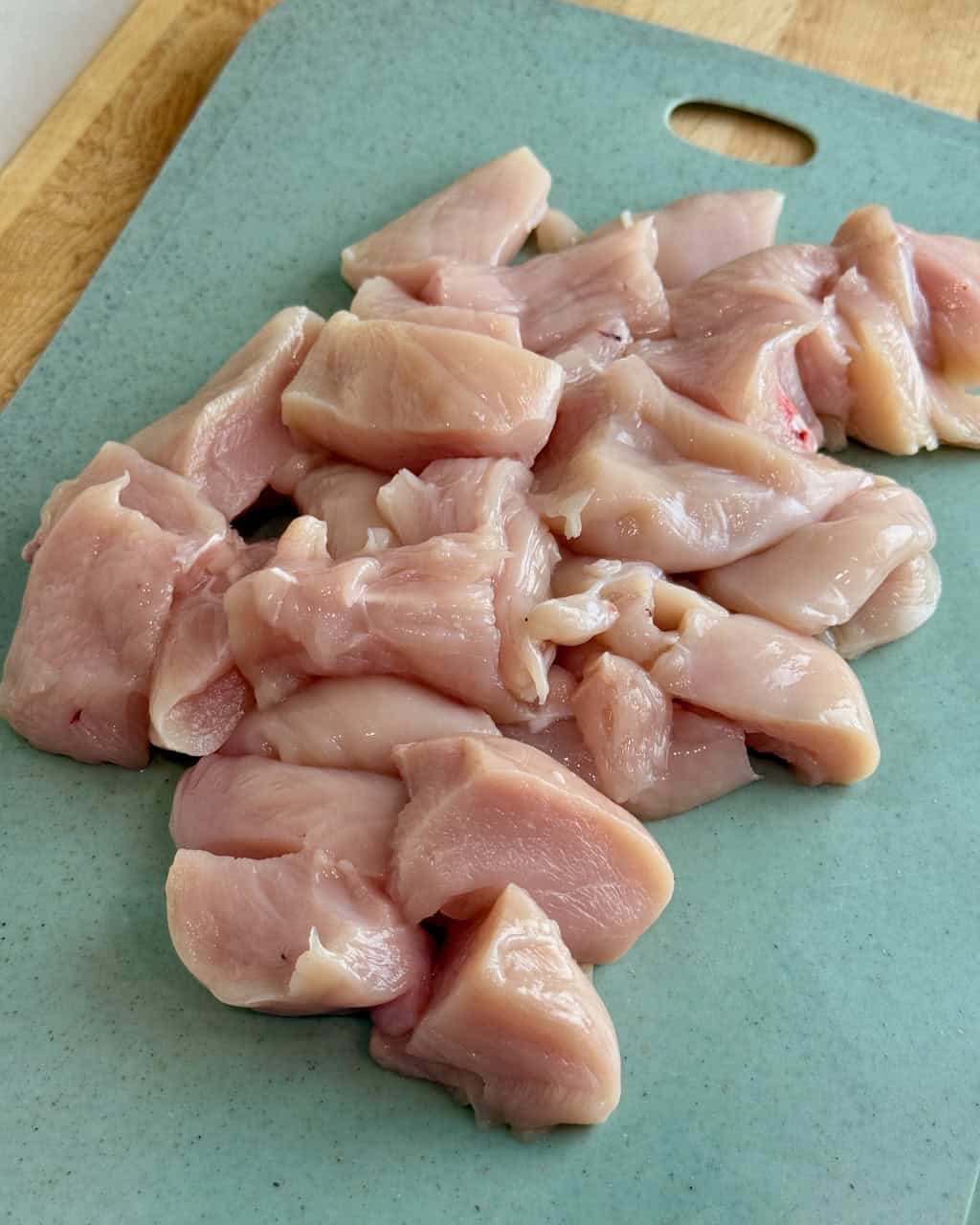 Boneless skinless chicken breast diced up on a cutting board.