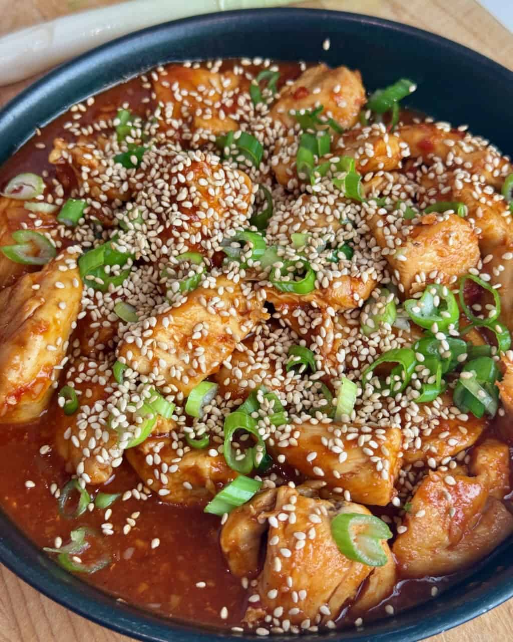 A plate of gochujang chicken with sesame seeds and green onions.