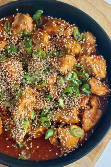 A plate of gochujang chicken with sesame seeds and green onions.