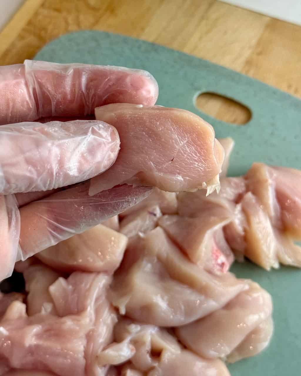 A woman holds a piece of raw chicken to show the size of the cubes.