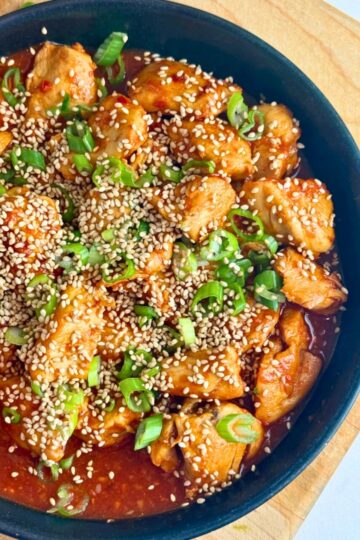 A plate of gochujang chicken with sesame seeds and green onions.