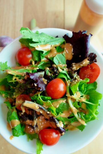 a bowl of green salad with gochujang tahini dressing with cherry tomatoes and drizzled on top.