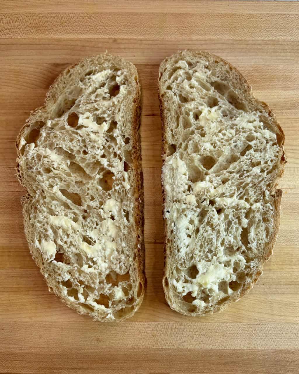 Two slices of buttered sourdough bread on a cutting board.