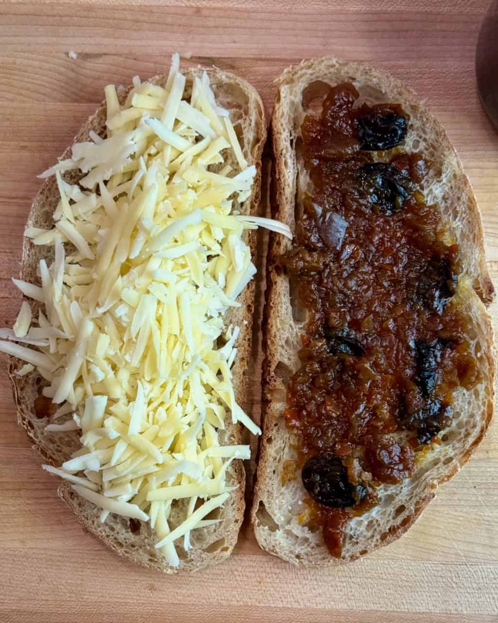 Two slices of sourdough bread with grated cheese on one side and chutney on the other.