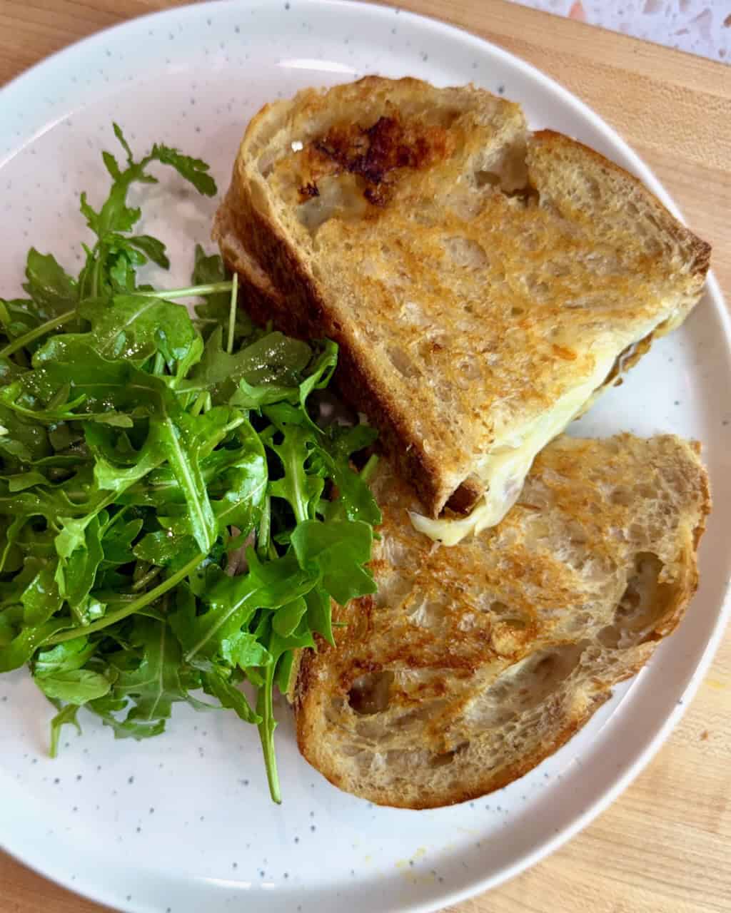 A grilled cheese and chutney sandwich with a side of arugula salad on a plate.