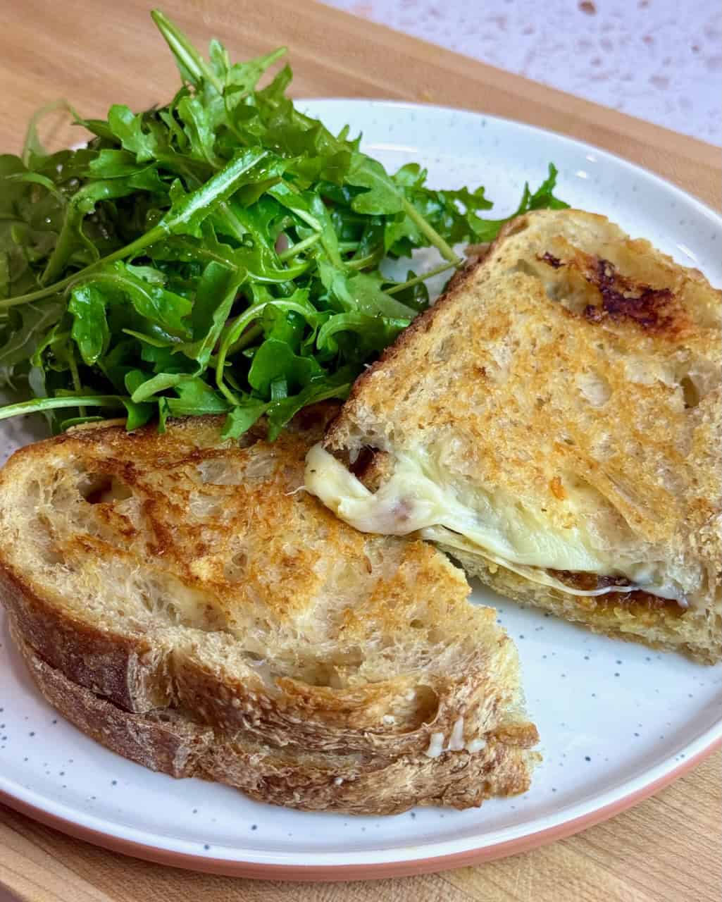 A grilled cheese and chutney sandwich with a side of arugula salad on a plate.