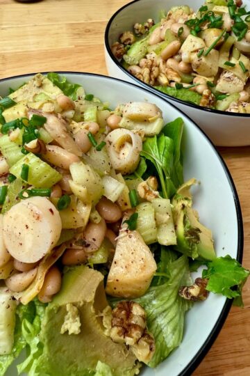 A large bowl of hearts of palm and white bean salad on a bed of arugula.