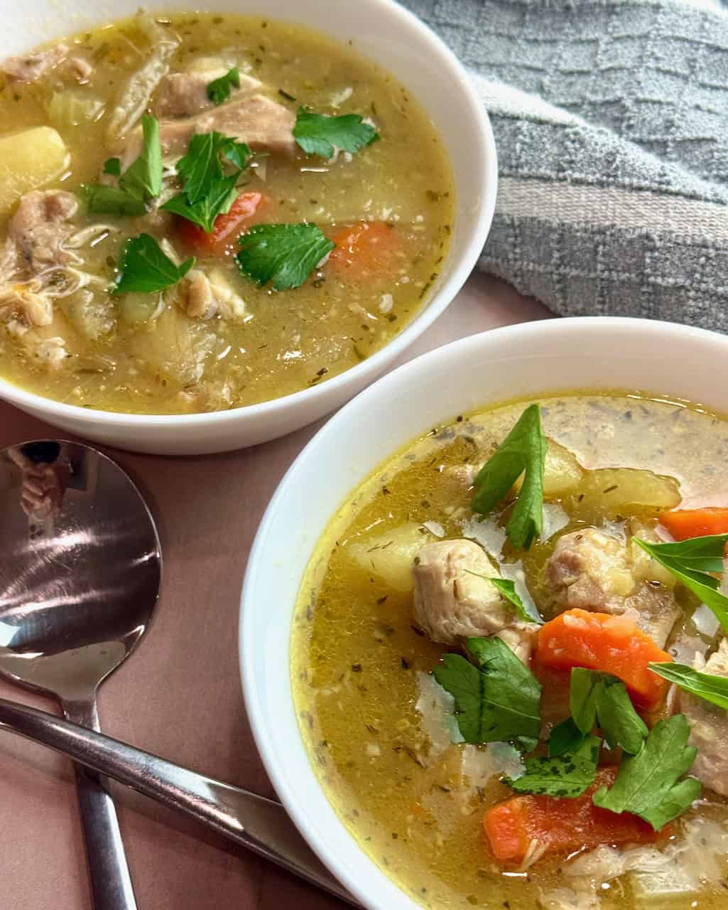 Two bowls of chicken stew with spoons beside them.