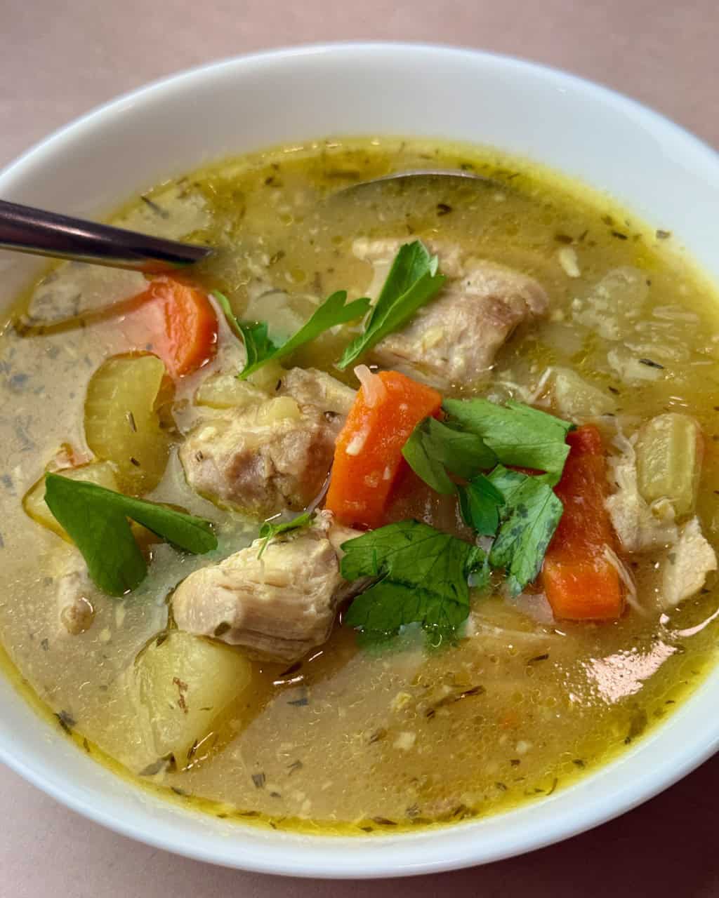 A bowl of chicken stew with a spoon in it.