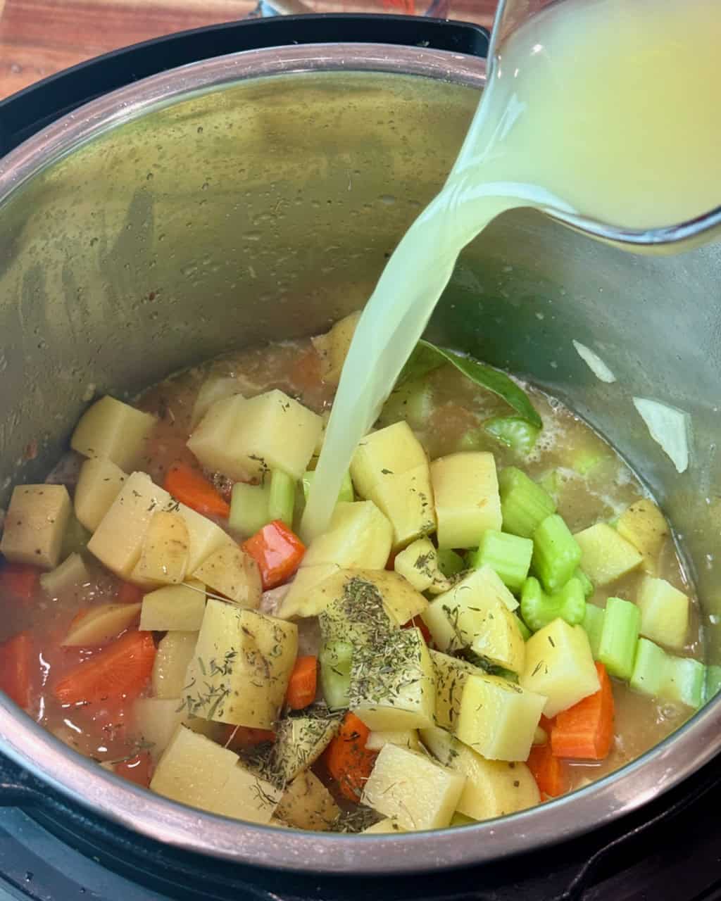 Adding chicken broth to the other ingredients in the pot.