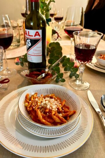 Romantic Italian dinner table setup with nduja pasta, flowers, and wine for a special night.