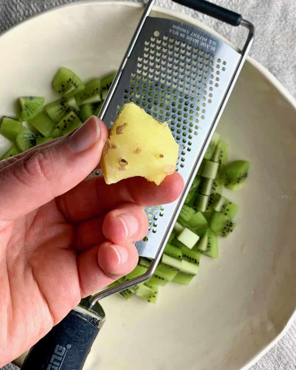 A woman prepares to grate a piece of ginger into a bowl of kiwi salsa.
