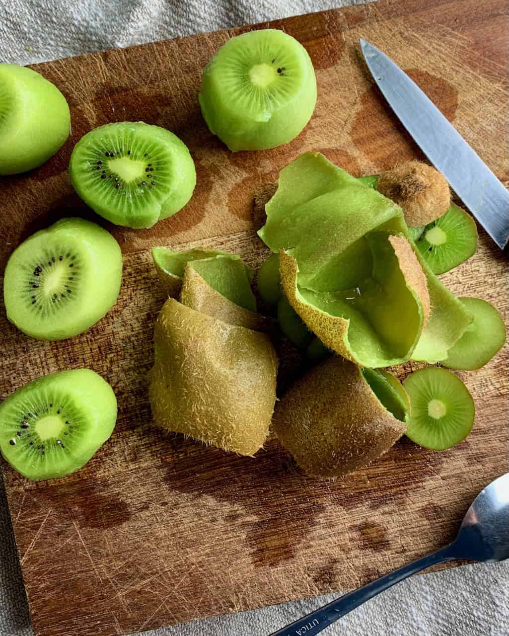Peeled kiwis and their trimmings on a cutting board.