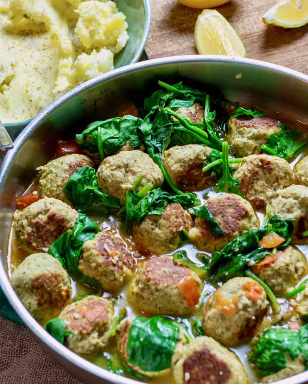 A pan full of brothy turkey meatballs with mashed potatoes and lemons.