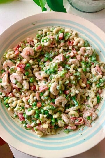 A woman holding a bowl of shrimp macaroni salad, ready to serve it up.