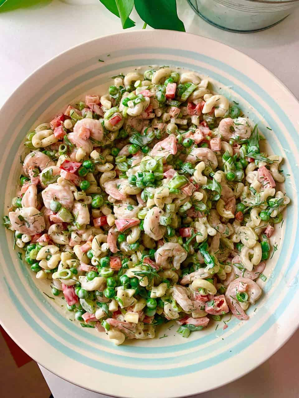 A woman holding a bowl of shrimp macaroni salad, ready to serve it up.