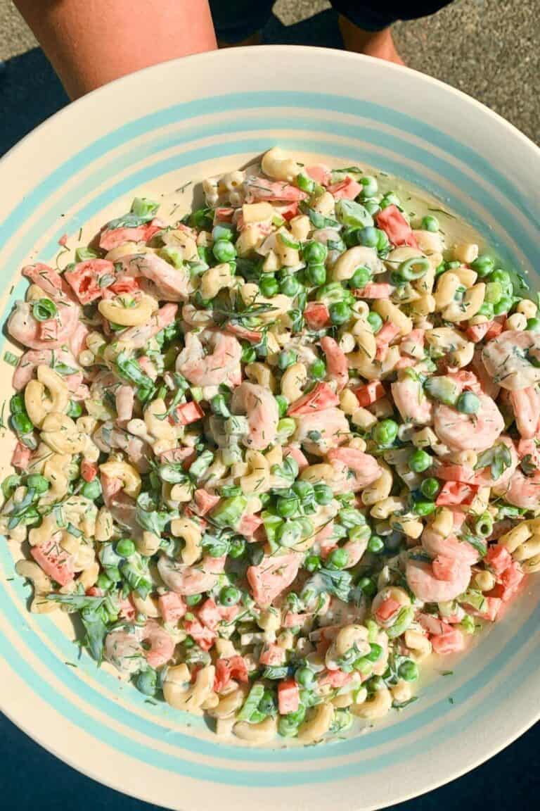 A woman holding a bowl of shrimp macaroni salad, ready to serve it up.