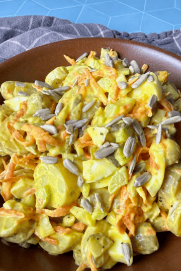 Classic potato salad in a brown bowl on a blue table with a grey napkin.