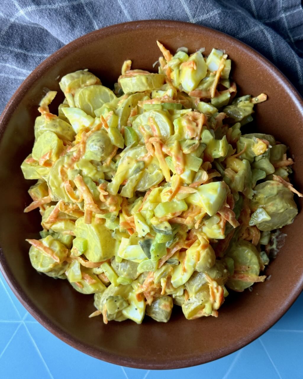 Classic potato salad in a brown bowl on a blue table.