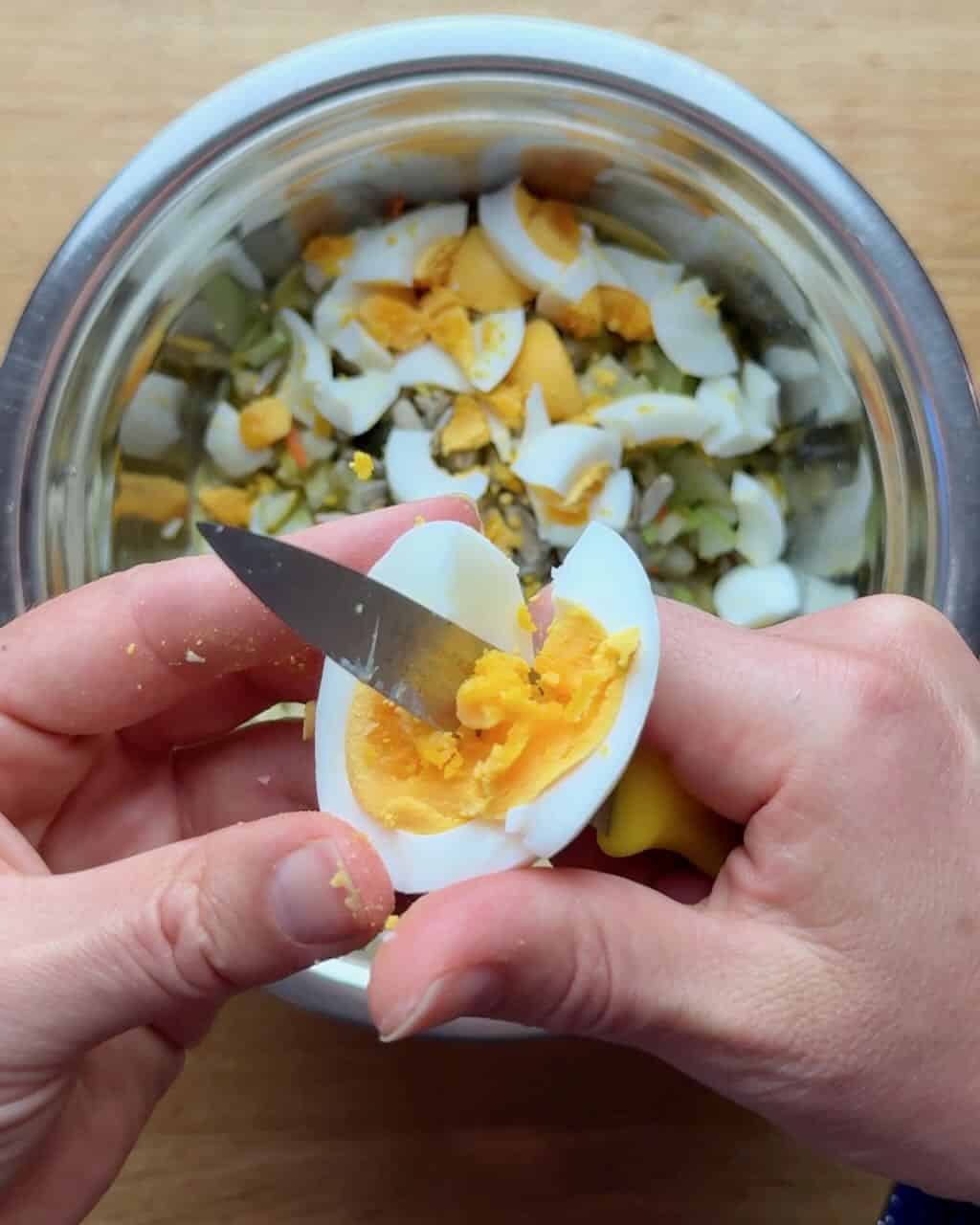 A woman chops hard boiled eggs into potato salad ingredients.