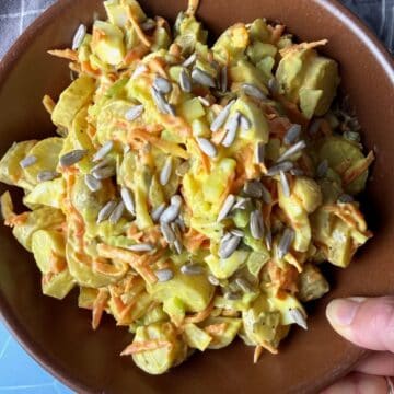 A woman holds a bowl of classic potato salad in a brown bowl on a blue table.
